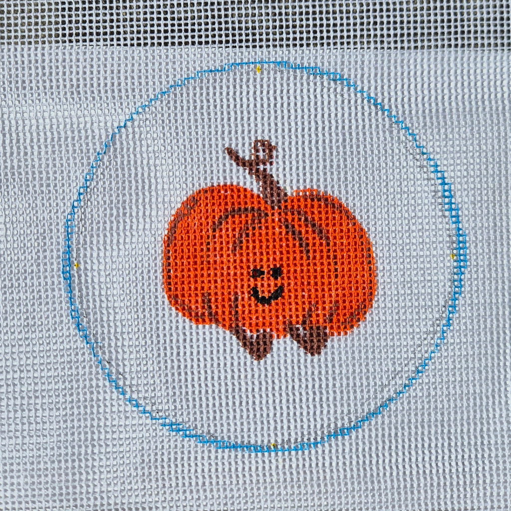 needlepoint pumpkin design on fabric with a blue circle border.